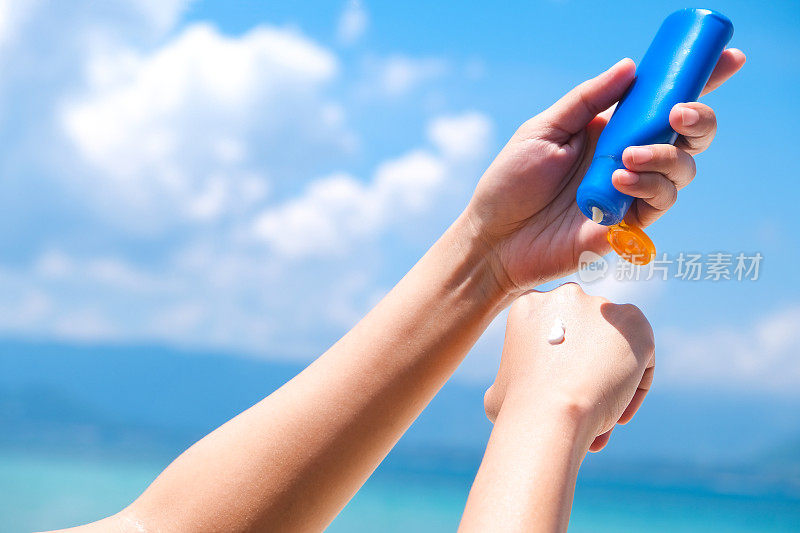 A woman is applying sunscreen and skin care to protect her skin from UV rays. 她正在手和胳膊上涂防晒霜。太阳标志是一个非常阳光的背景。健康护肤理念